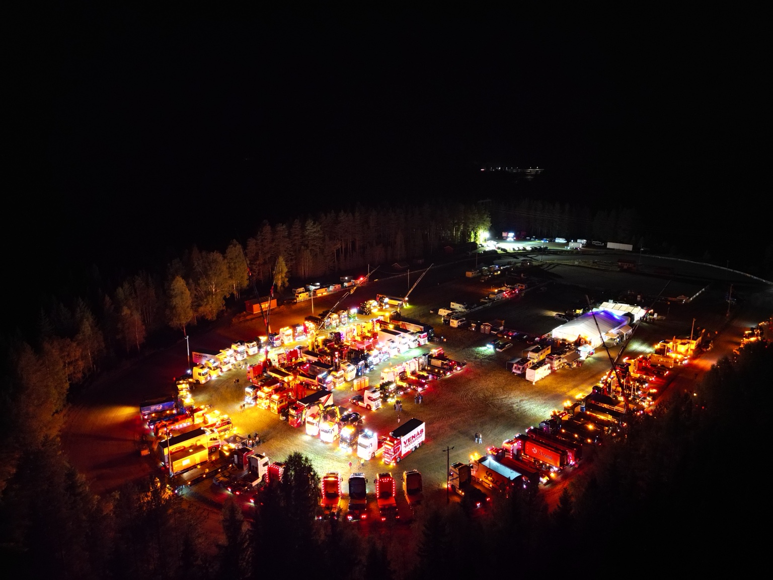 Oversiktsbilde av festivalområdet om kvelden med opplyste lastebiler og festivaltelt.