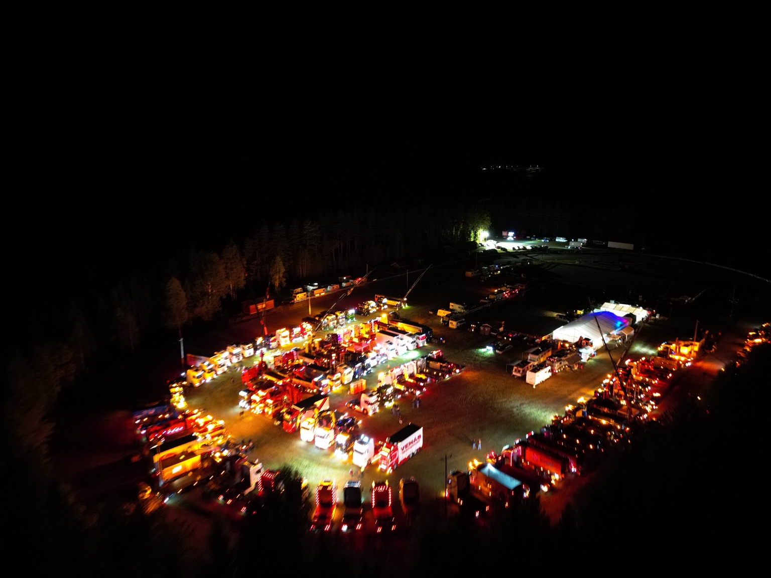 Festivalområdet sett ovenfra om natten, med lys fra lastebiler og festivaltelt.