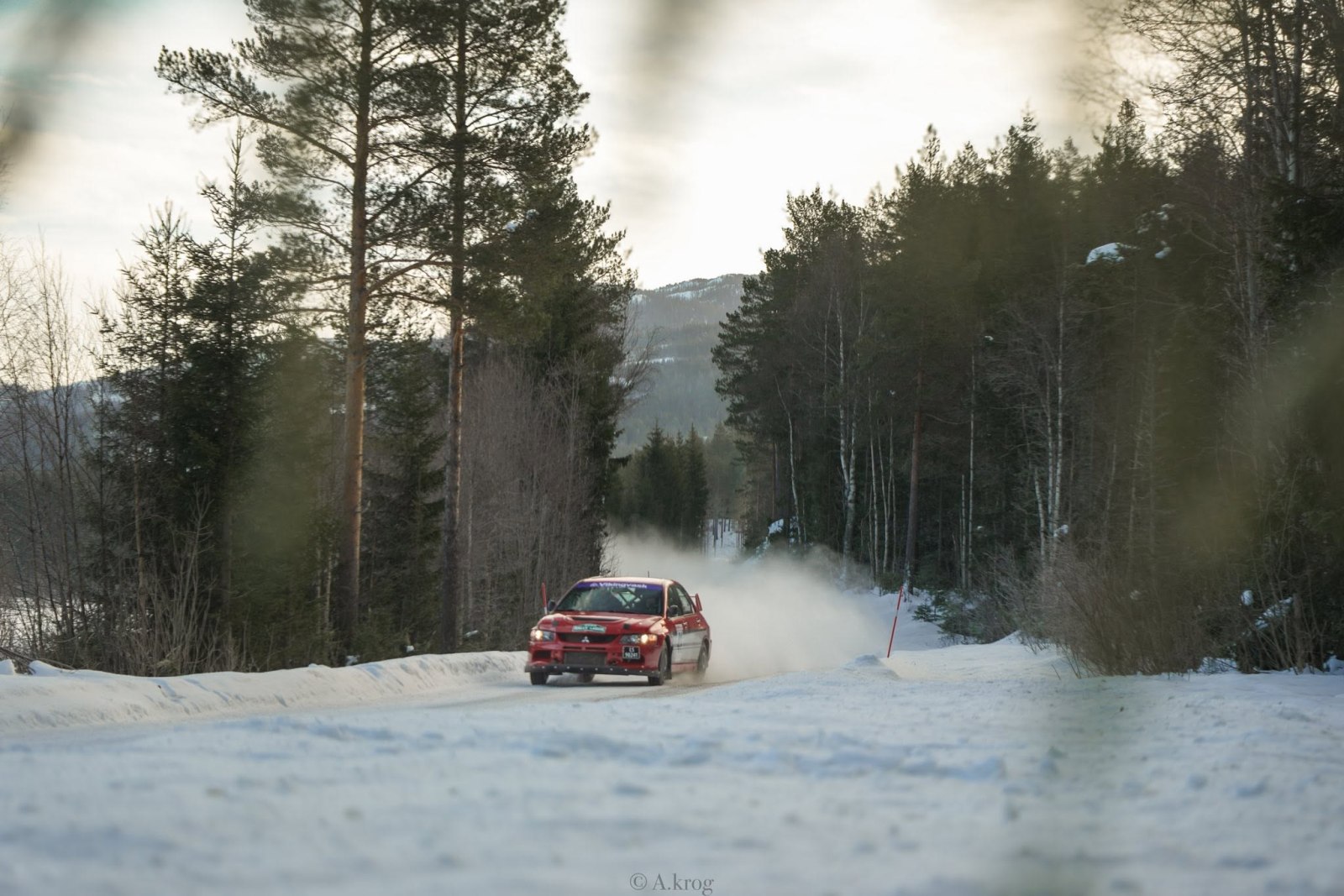 Rød rallybil på snødekt skogsvei.