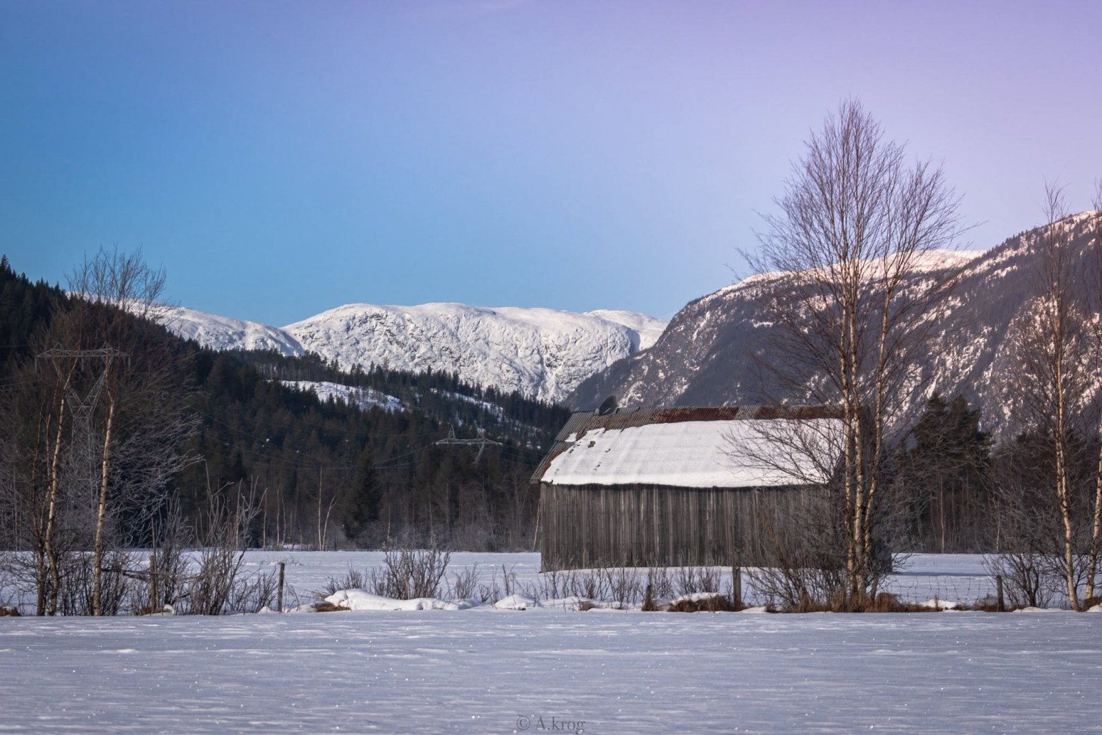 Vinterlandskap med låve og snødekte fjell.